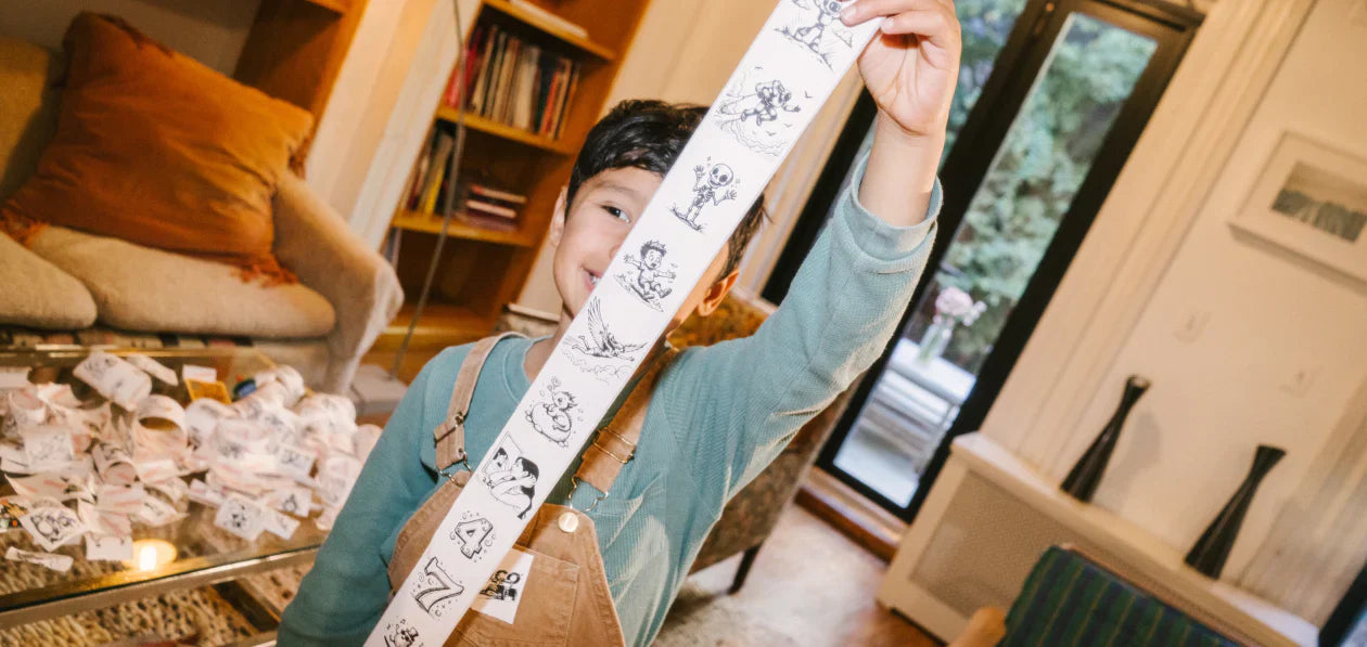 a boy holding up a long strip of printed stickers featuring various black-and-white illustrated characters and animals