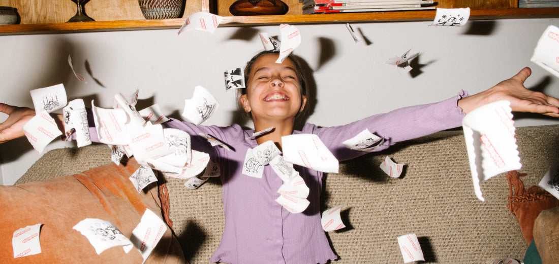 A child sitting on a couch joyfully throwing stickers into the air.