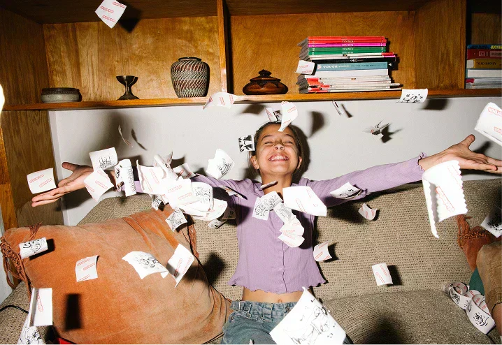 A child sitting on a couch joyfully throwing stickers into the air.
